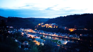 A historic town with a river, surrounded by hills and featuring illuminated buildings and a castle-like structure.