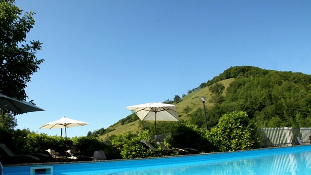 A swimming pool with lounge chairs and umbrellas, surrounded by greenery and hills. - Selvicolle Country House (Castelraimondo)