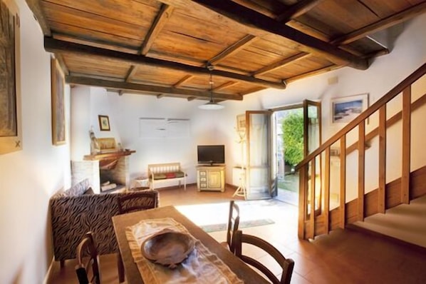 Uma sala de estar espaçosa com teto de madeira, uma área de jantar com mesa e cadeiras, uma televisão e uma escada que leva a outro nível.