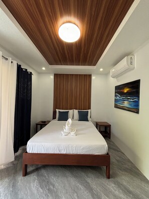 A hotel room with a wooden ceiling, a bed with white linens, two pillows, a painting of a sunset, and an air conditioning unit. - Alona Grove Tourist Inn (Panglao)