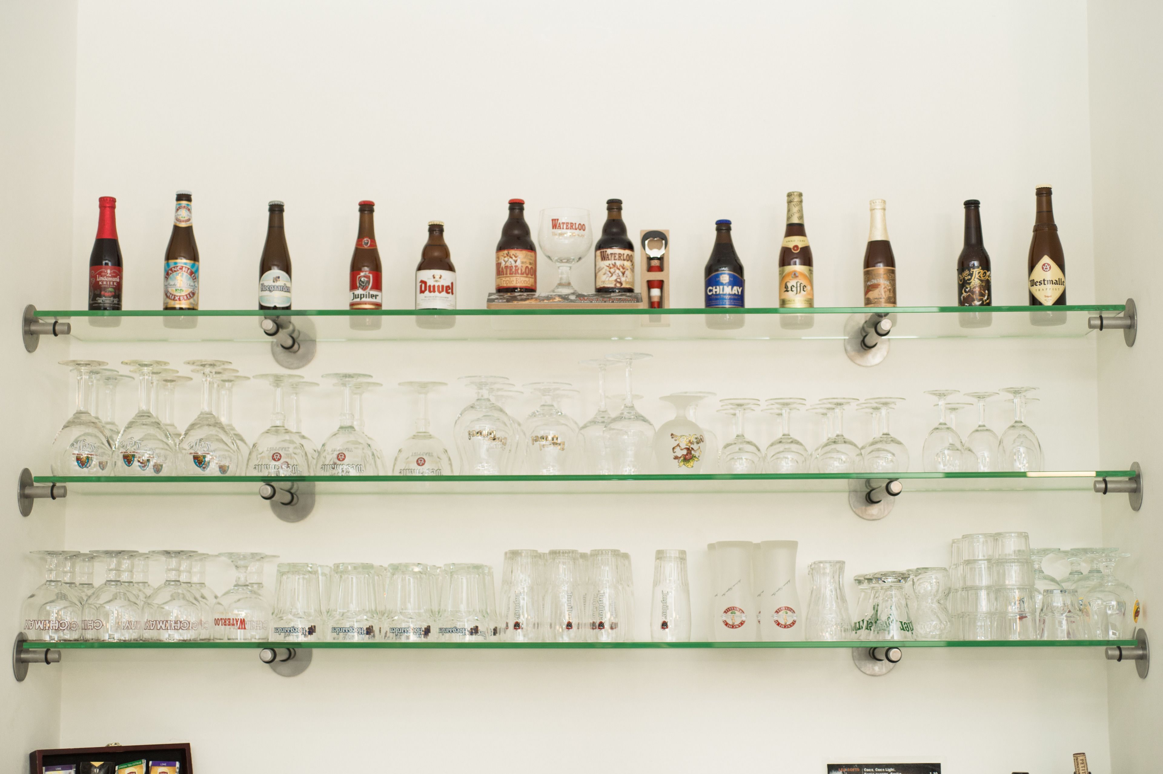 Een muur met drie planken waarop verschillende flessen en glazen staan.