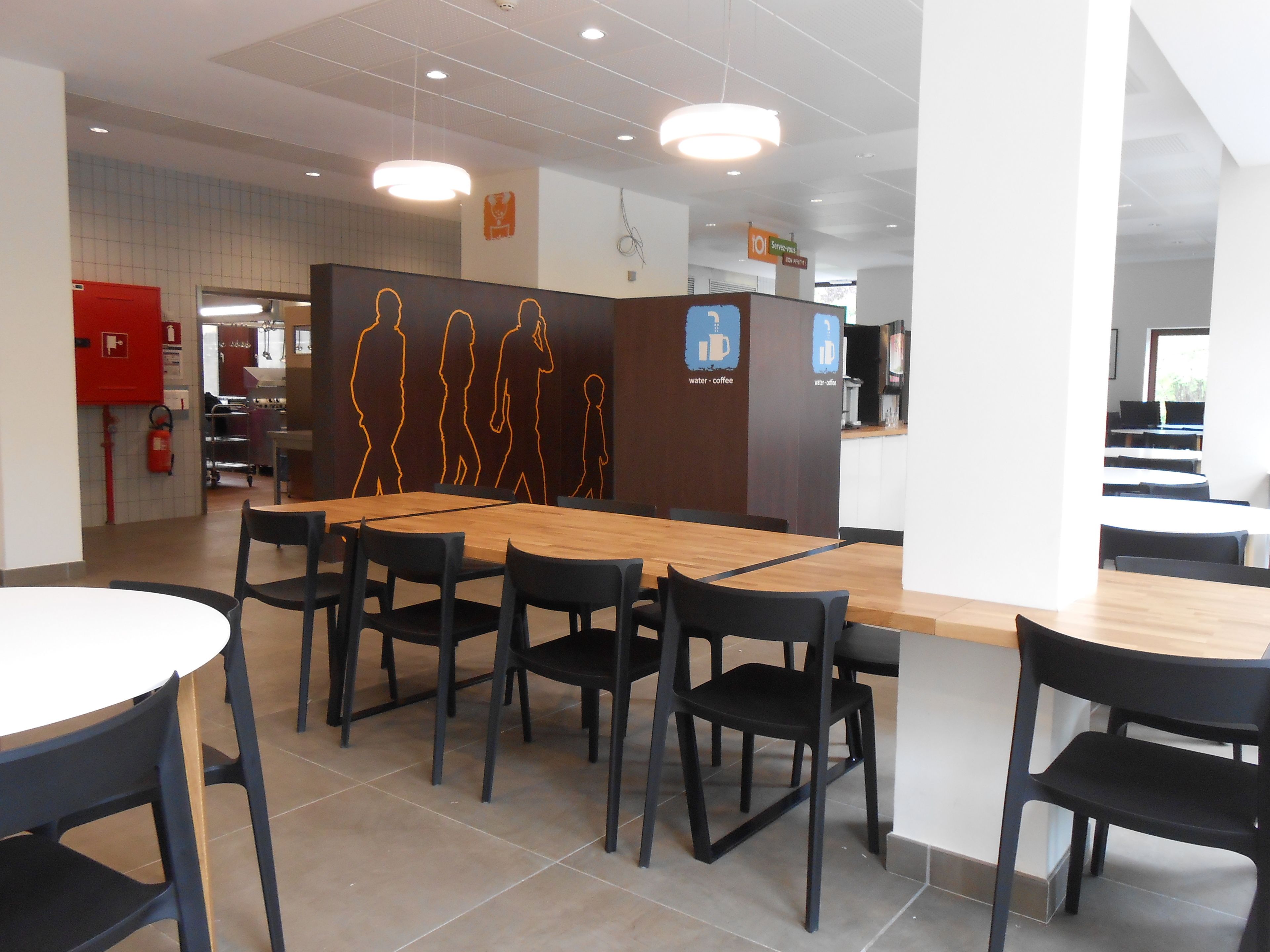 A modern cafe with a wooden counter, black chairs, and a tiled floor.