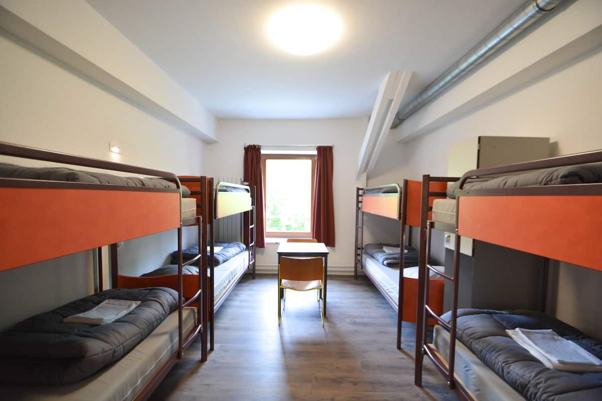 A dormitory room with bunk beds, a desk, and a chair.