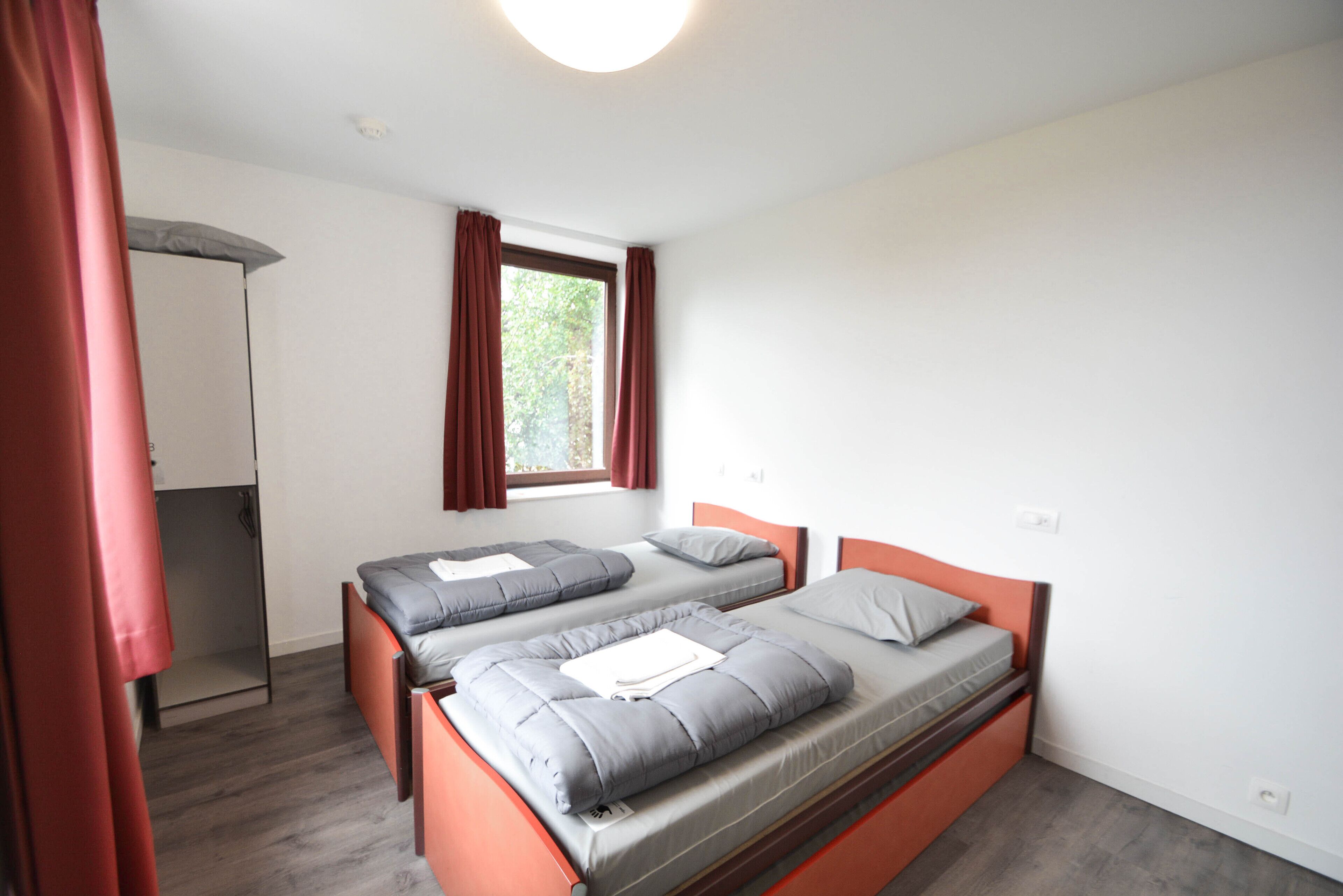 A bedroom with two beds, a window with curtains, and a mirror.