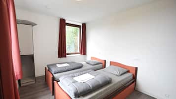 A bedroom with two beds, a window with curtains, and a mirror.