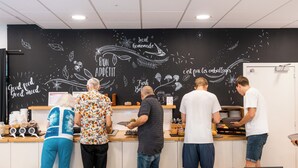 Un café dont un mur est recouvert d’un tableau noir où sont écrits des slogans et dessinés des motifs sur le thème de la nourriture.