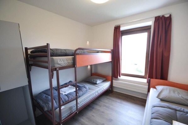 Un dormitorio con literas, una ventana con cortinas y suelo de madera.