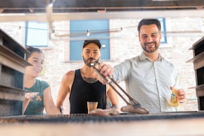 En person som grillar utomhus med en tegelvägg och fönster i bakgrunden.