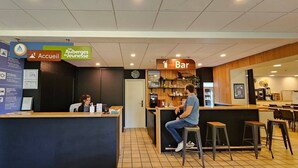 Un comptoir d’accueil avec une enseigne indiquant « Accueil » et « Auberges de jeunesse », un espace bar avec des tabourets et un comptoir sur lequel se trouve une horloge.