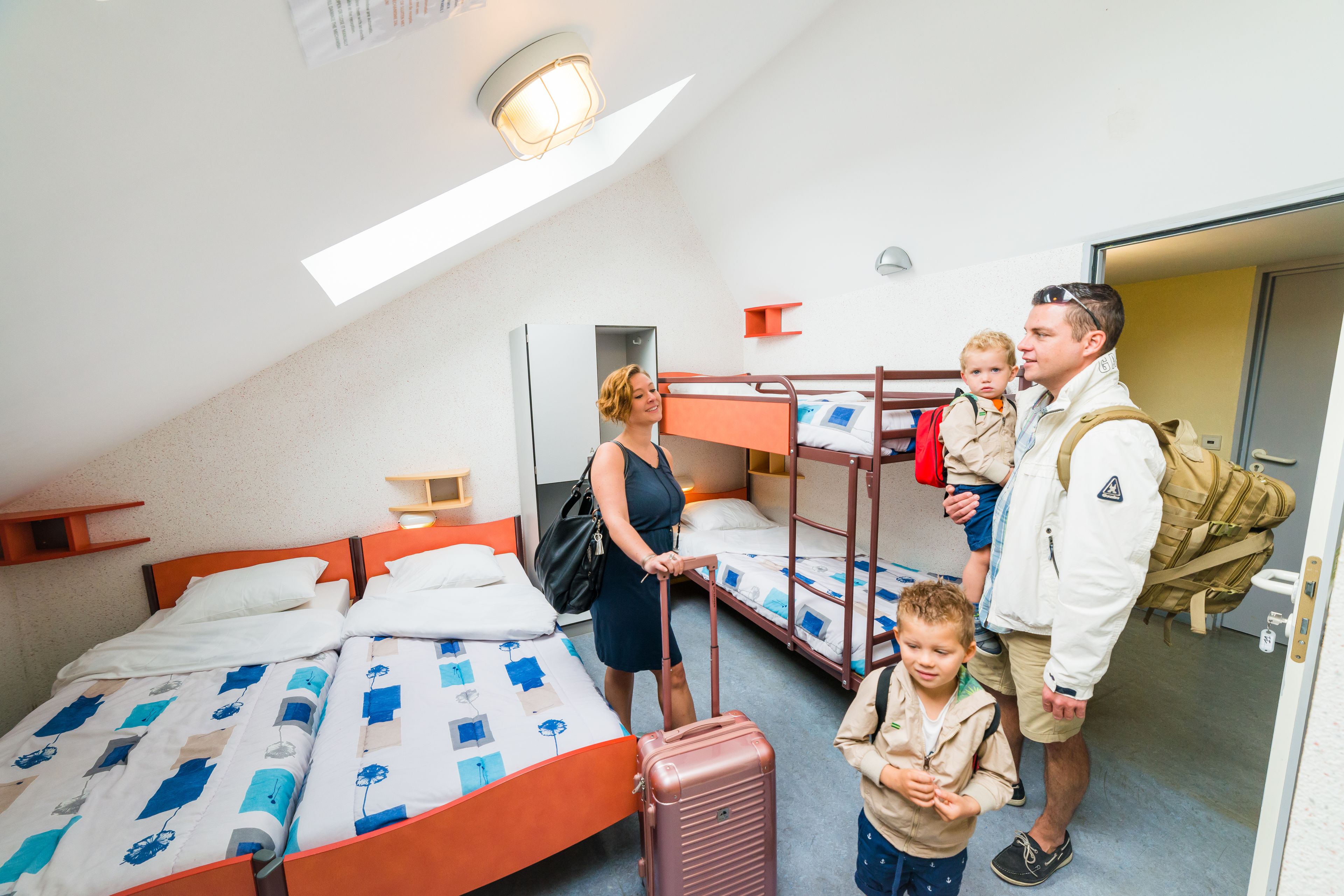 Een kamer met stapelbedden, een koffer en een persoon die een kind vasthoudt.