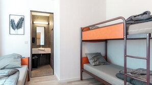 Une chambre avec un lit superposé et un lit simple, et une salle de bain visible à travers une porte ouverte.