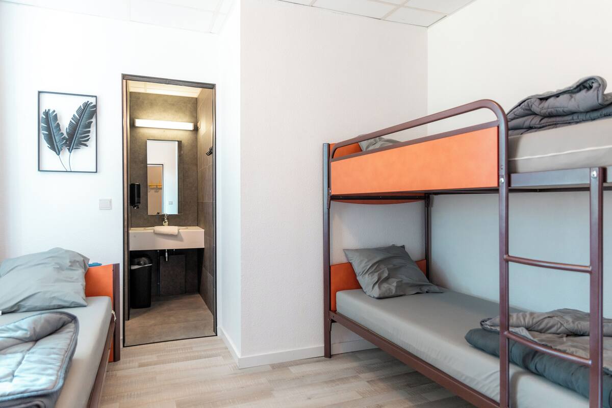 A bunk bed room with a single bed and a bathroom visible through an open door.