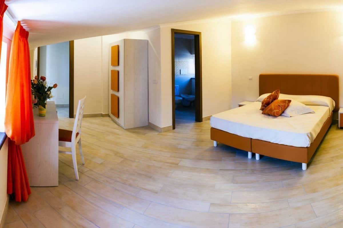 A hotel room with a bed, a desk, a chair, a suitcase, and a bathroom visible through an open door.