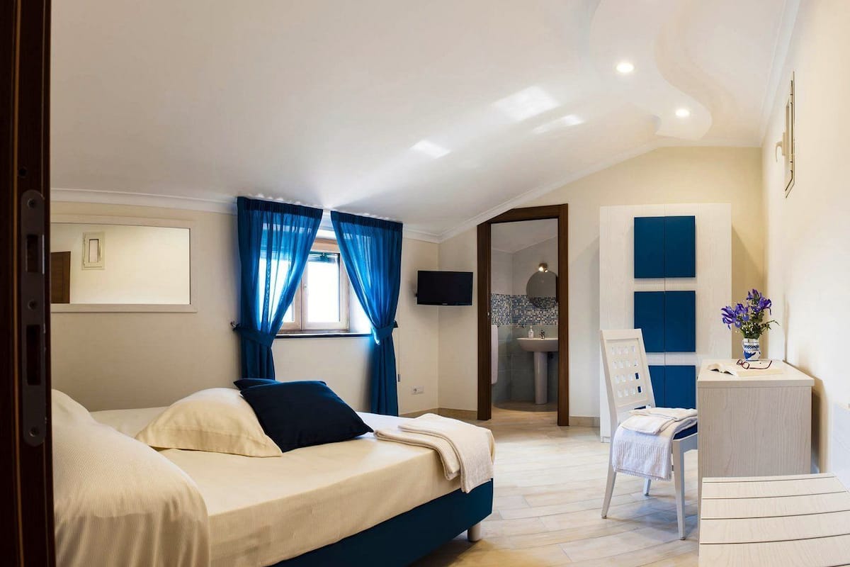 A bedroom with a bed, a desk, and a bathroom visible through an open door.