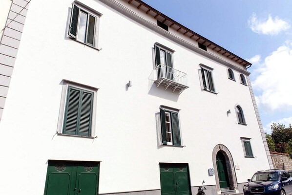 A white building with green shutters, a balcony, and a green door.