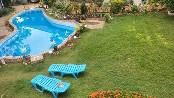 Una piscina con bordo curvo, circondata da un cordolo in pietra e piante in vaso. Due poltrone blu sono posizionate sull'erba.