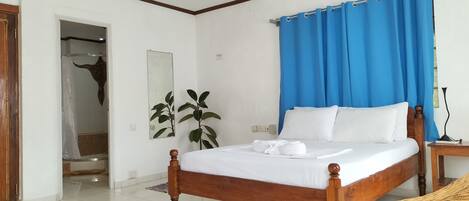A bedroom with a wooden bed, white bedding, a blue curtain, and a mirror on the wall.