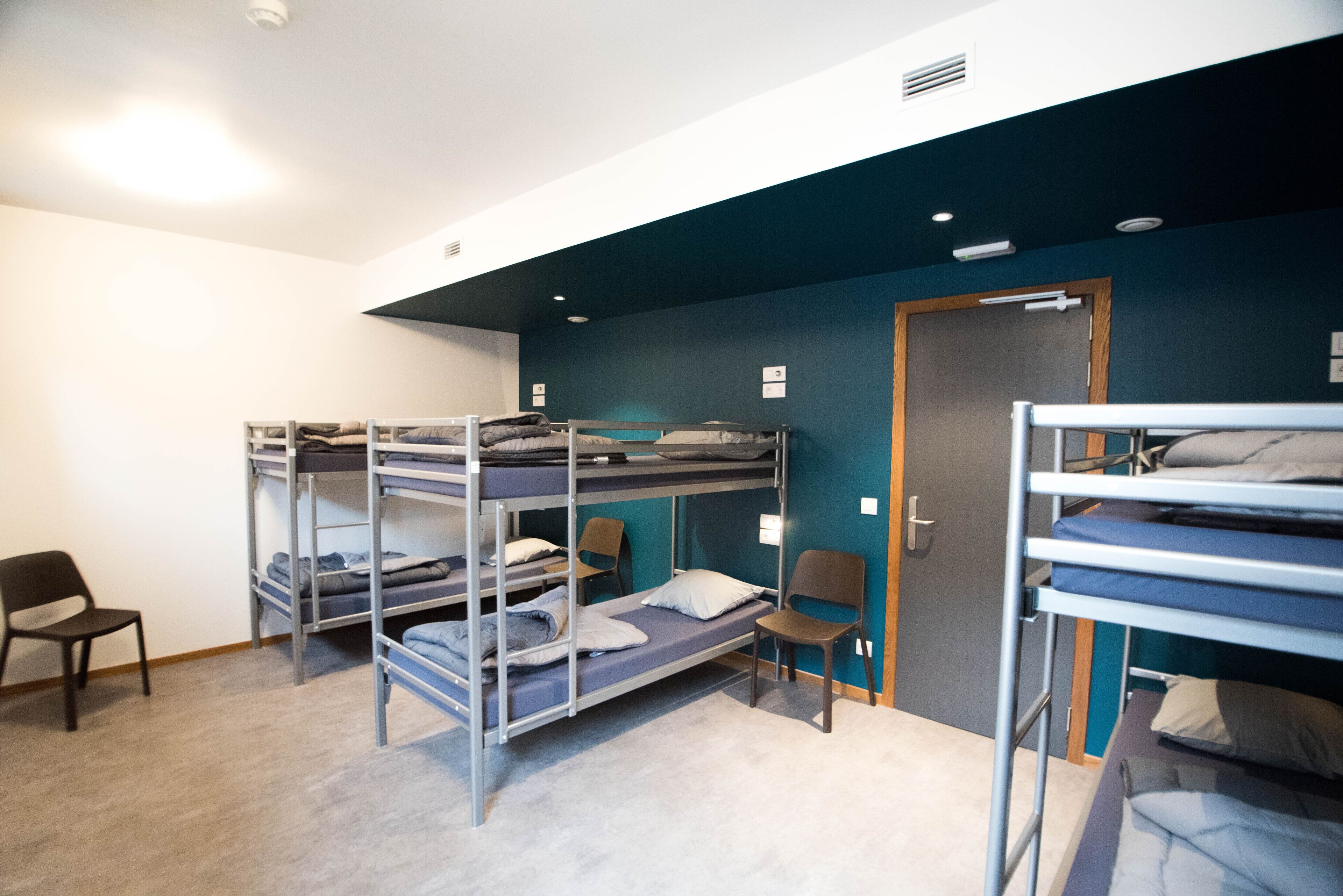 Una habitació de dormitori amb llits superposats, cadires i una porta.
