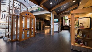 A spacious lobby with a wooden reception desk, a glass door entrance, and a seating area with a television. - Liège Youth Hostel (Liege)