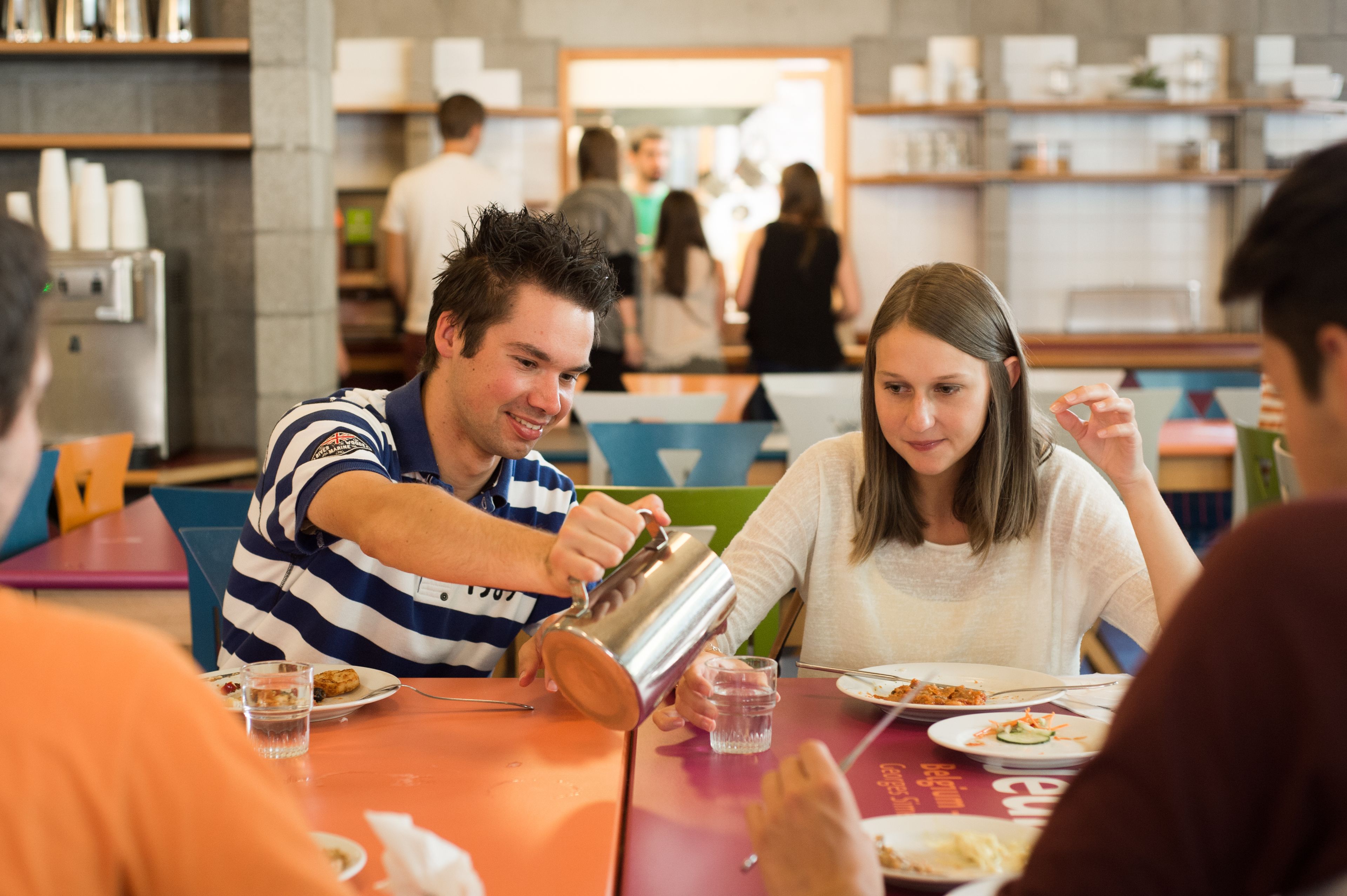 A group of people dining at a restaurant with a modern interior, including a counter and shelves with various items.