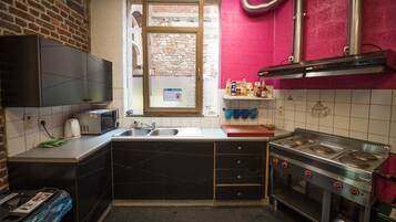 Une cuisine compacte équipée d’un four à micro-ondes, d’un évier et d’une cuisinière. Une fenêtre donne sur un mur de briques à l’extérieur.