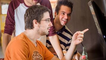 Drie personen zitten aan een tafel met een computer, een toetsenbord en een muis.
