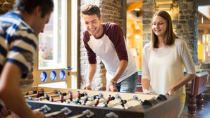 A group of people playing foosball in a room with brick walls and large windows. - Liège Youth Hostel (Liege)