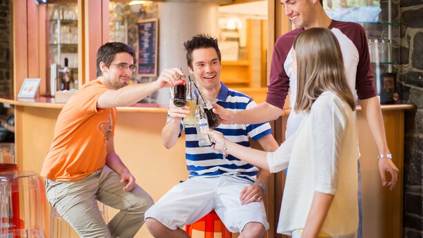 A group of people sitting and standing in a bar area with stools and a counter. - Liège Youth Hostel (Liege)