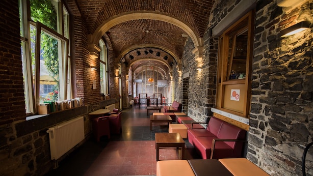 A cozy interior with stone walls, wooden benches, and tables arranged in a corridor. - Liège Youth Hostel (Liege)