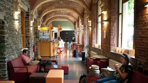A spacious lobby with high arched brick ceilings, comfortable seating areas, and a bar in the background. - Liège Youth Hostel (Liege)