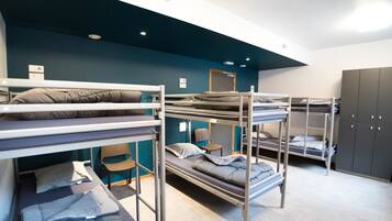 Um quarto em dormitório com beliches, uma escrivaninha e um guarda-roupa.