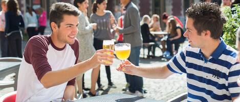 Dos personas brindan con bebidas en una mesa al aire libre con un teléfono inteligente encima.
