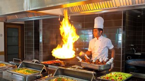 A buffet with various dishes, a chef performing a flambé, and a large wok in the background. - Club Mermaid Village  (Alanya)