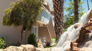A hotel with a waterfall, palm trees, and a pool. - Club Mermaid Village  (Alanya)