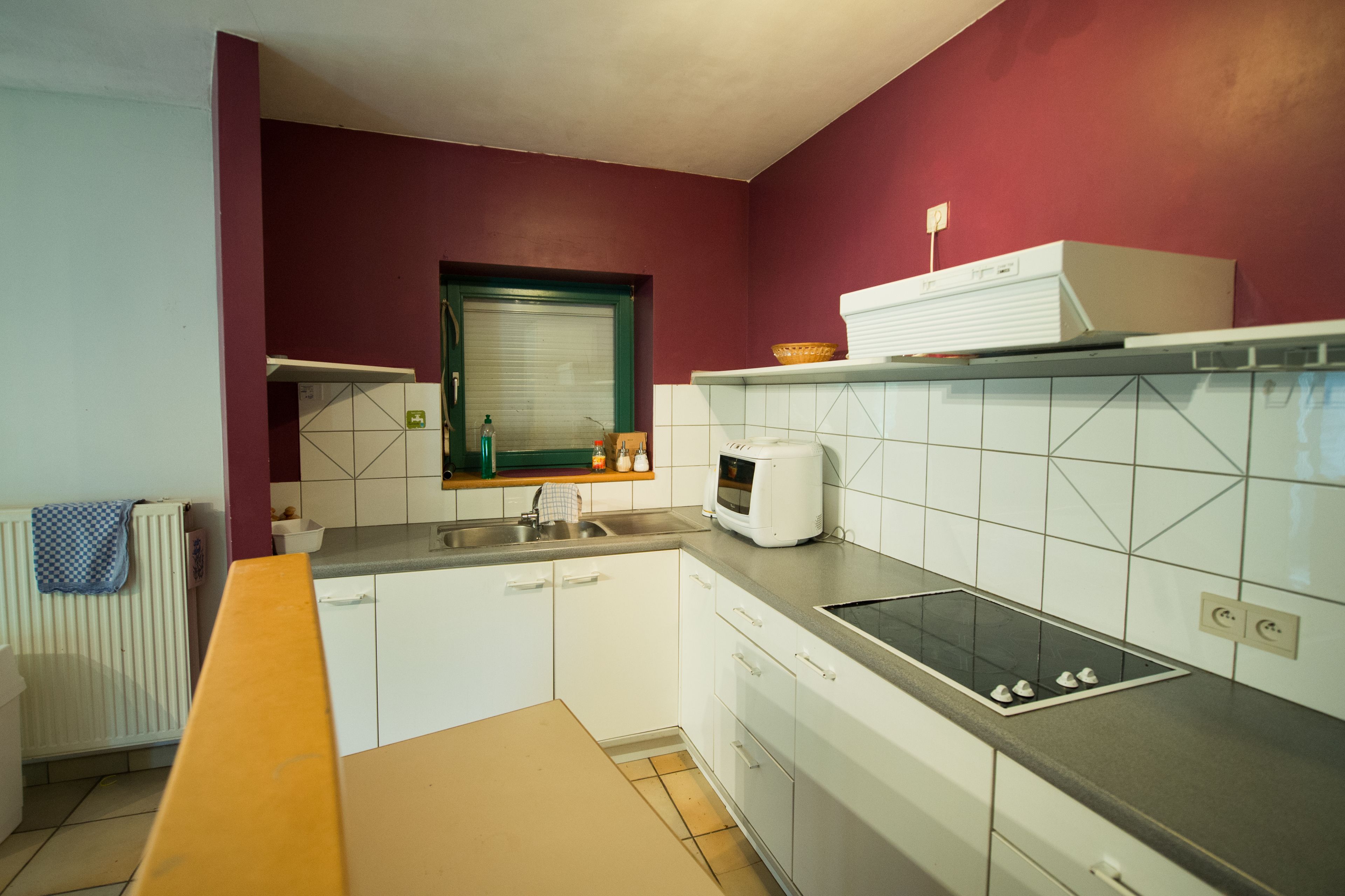 Una cocina con armarios blancos, un microondas, un lavamanos y una ventana con marco verde.
