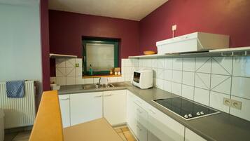 Una cocina con armarios blancos, un microondas, un lavamanos y una ventana con marco verde.