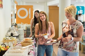 Una mesa de buffet con diversas opciones de comida y un grupo de personas reunidas alrededor.