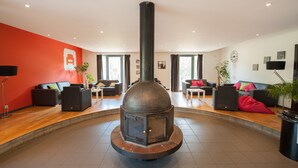 A modern living room with a central wood-burning stove, comfortable seating, and a red accent wall. - Malmedy Youth Hostel (Malmedy)