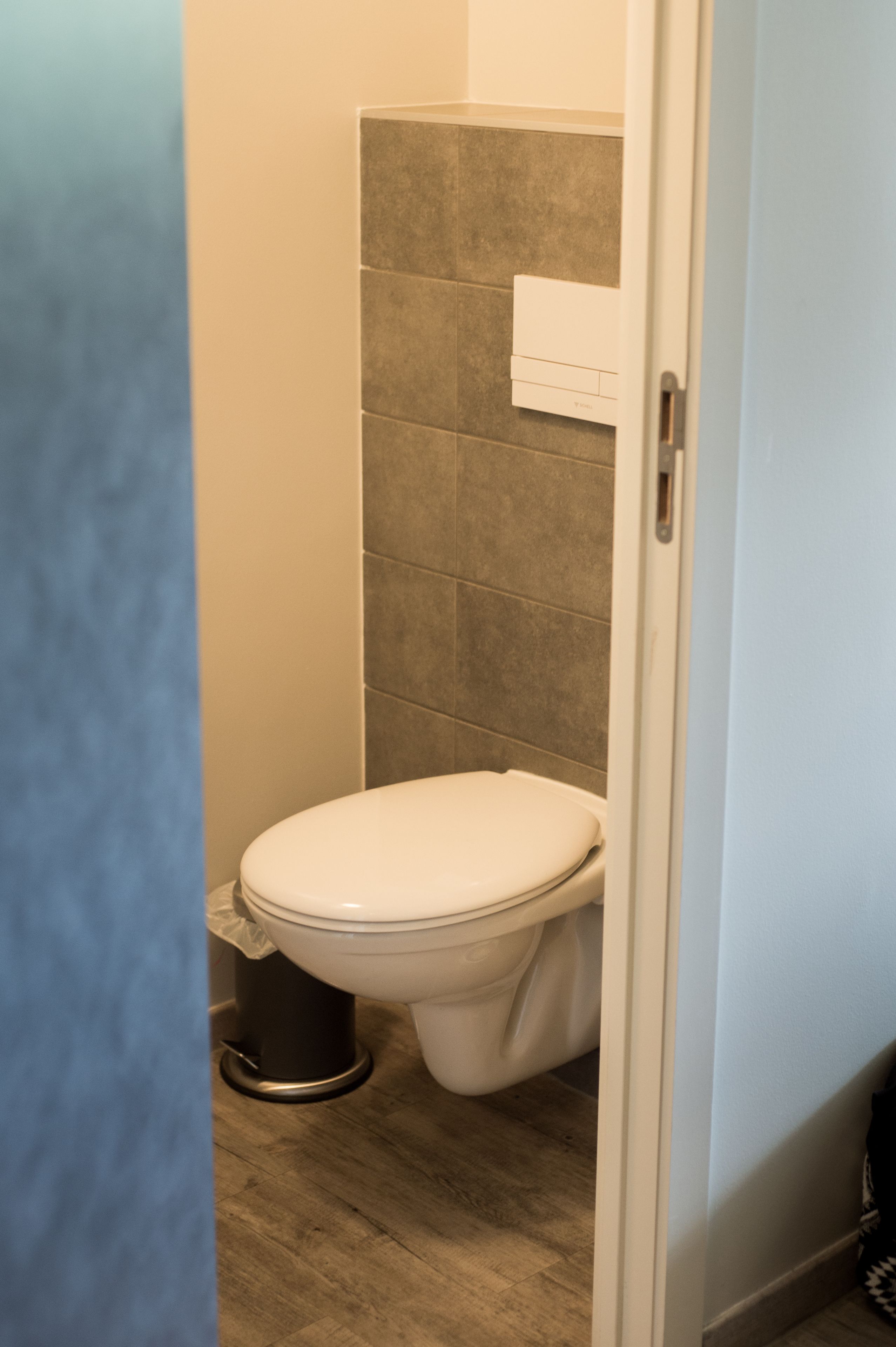 Un baño pequeño y funcional con inodoro, un cubo de basura y una toalla colgada en la pared.
