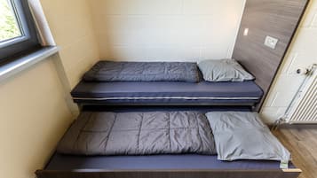 A compact room with two single beds, each with a mattress and pillow.