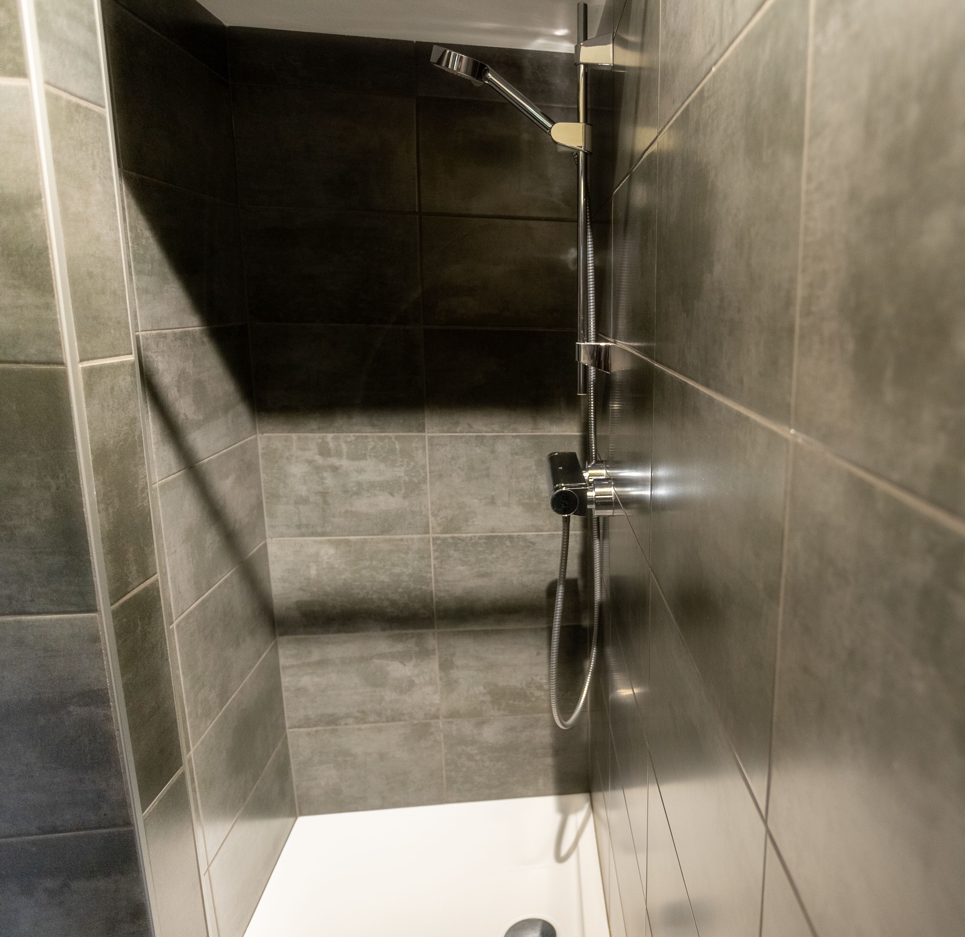A modern bathroom with a shower, tiled walls, and a visible drain.