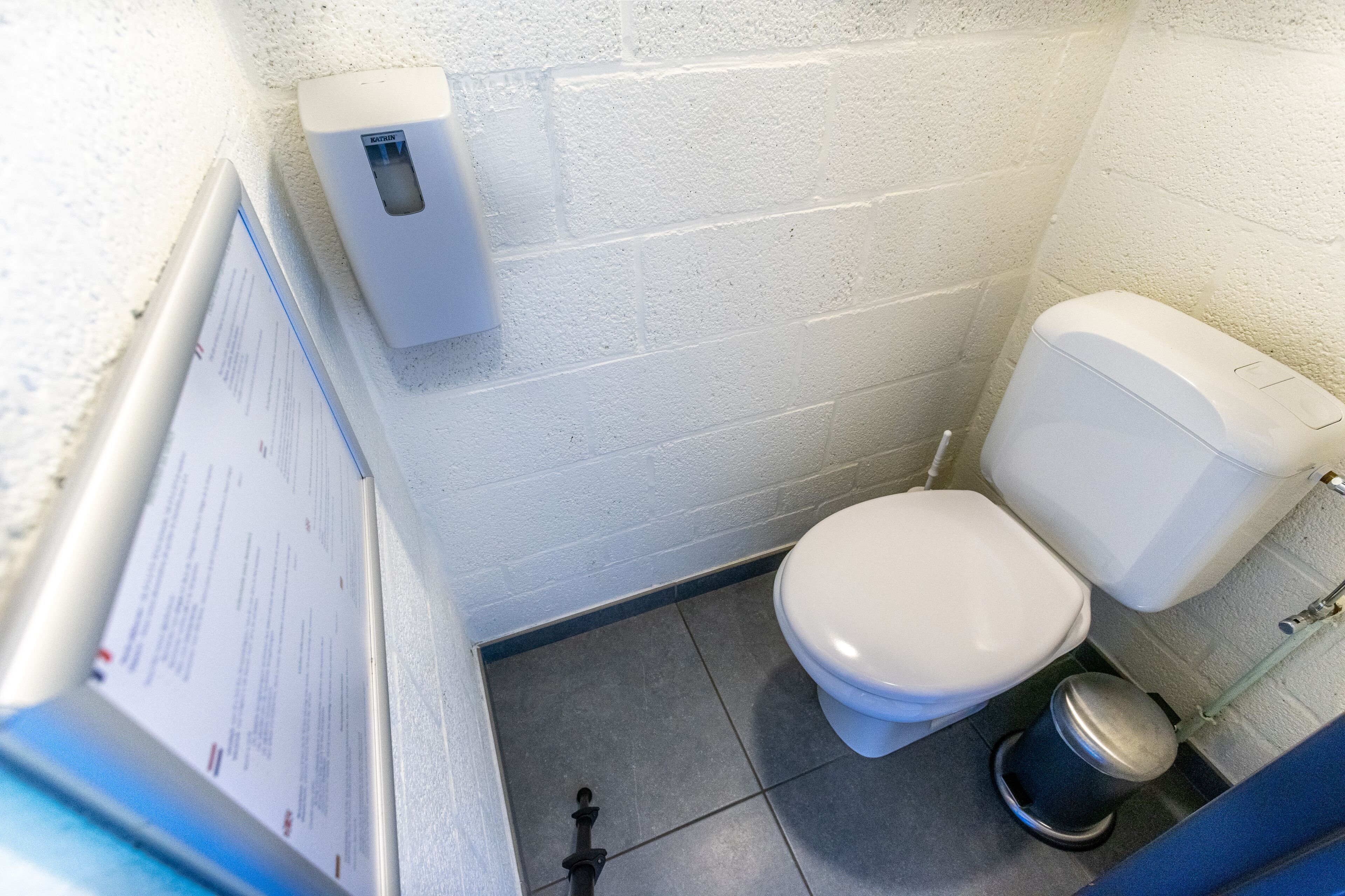 Une petite salle de bain propre, avec des toilettes, une poubelle et un distributeur de savon fixé au mur.