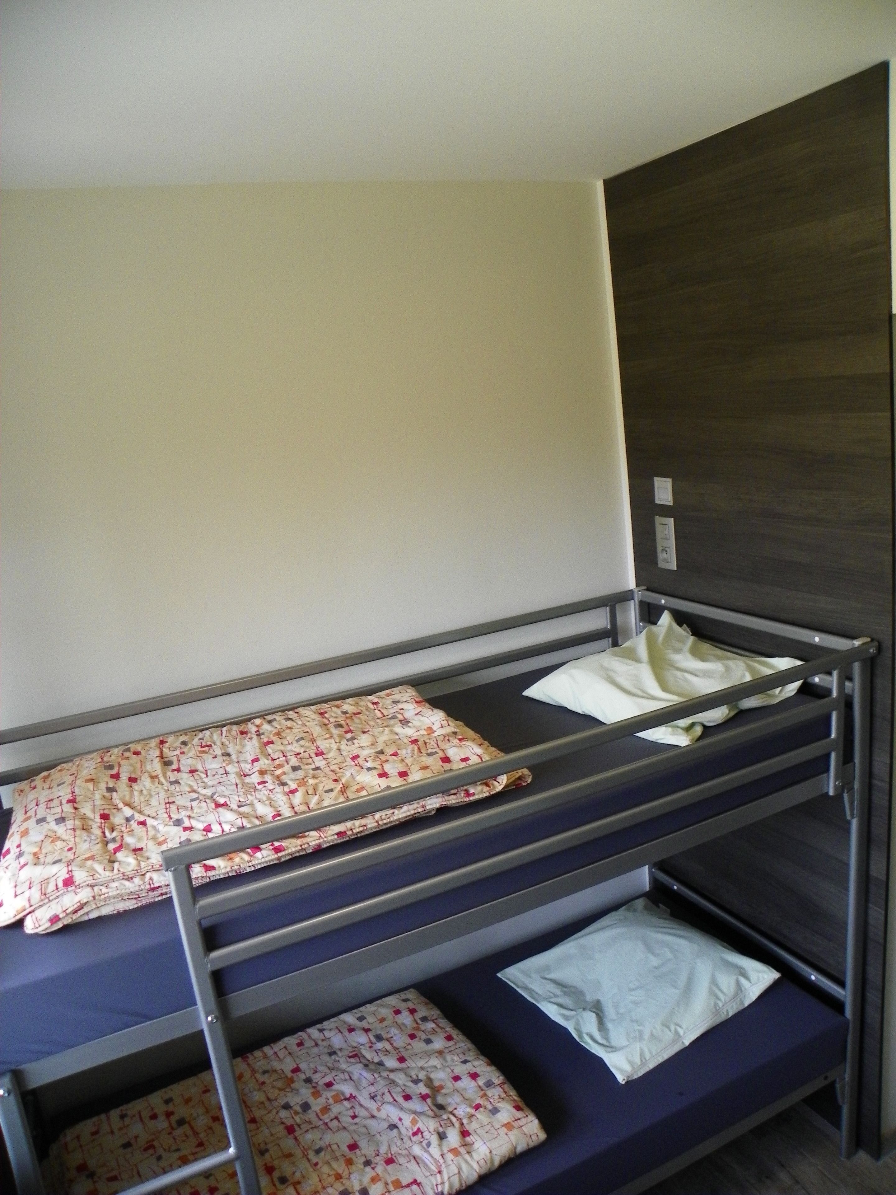 Un lit superposé à deux niveaux, un mur uni et un panneau en bois foncé sur le côté droit.