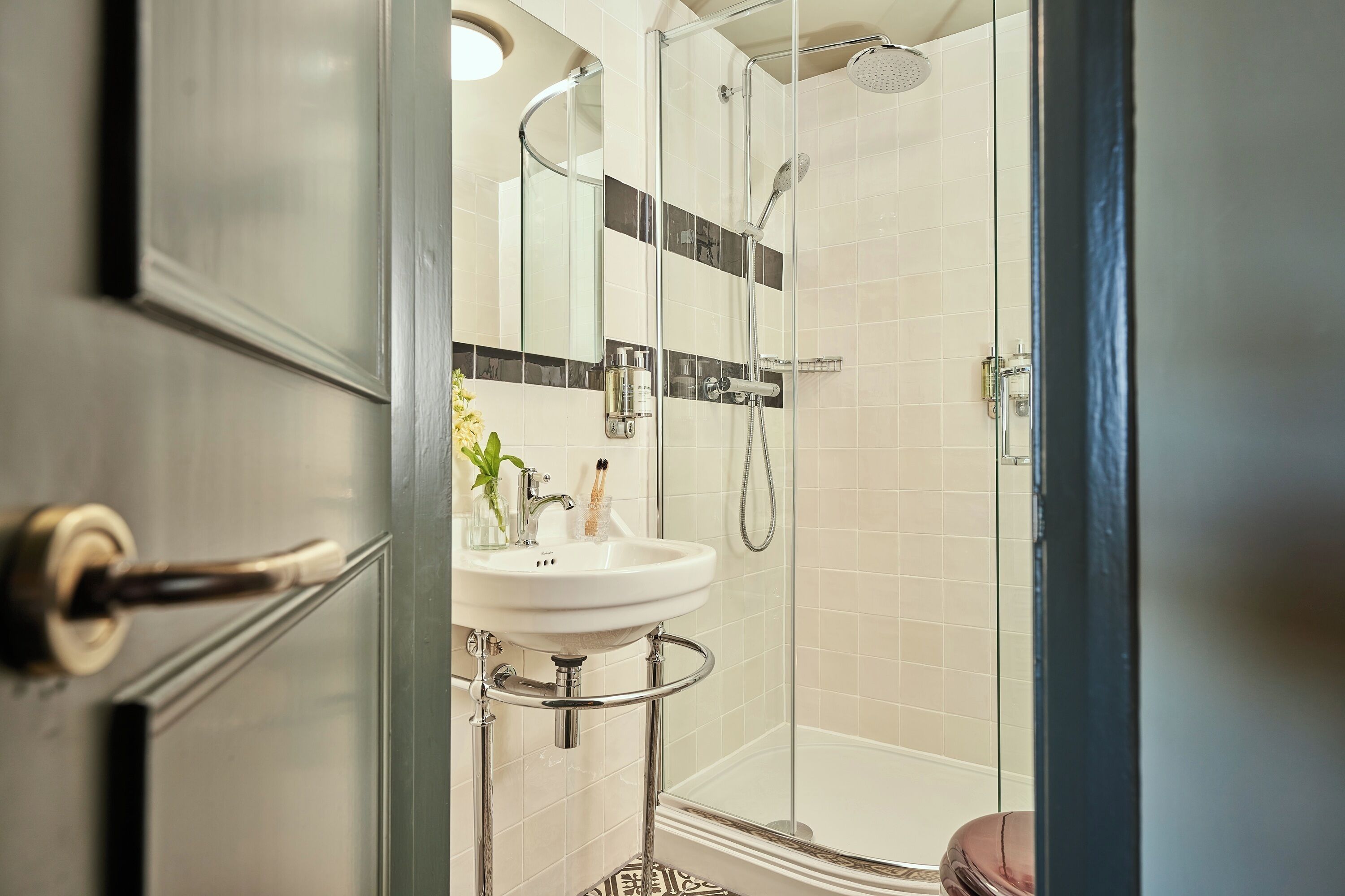 Un baño moderno con cabina de ducha de vidrio, lavamanos blanco y puerta de vidrio.