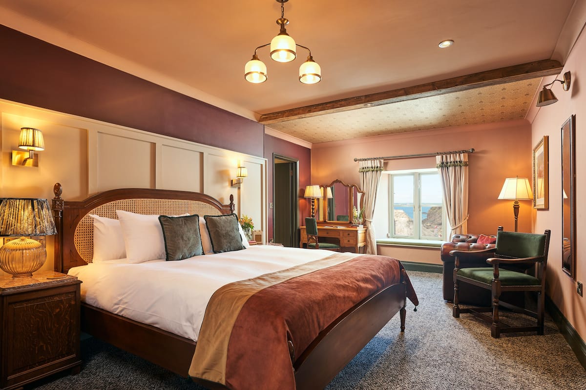 Ein gut beleuchtetes Hotelzimmer mit einem großen Bett, einem Schreibtisch, einem Stuhl und einem Vorhangfenster.