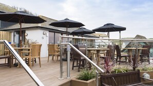 A wooden deck with outdoor seating, including tables and chairs, and multiple umbrellas providing shade. - Hope & Anchor (Kingsbridge)