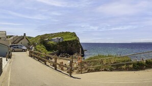 A coastal road leading to a beach with thatched-roof cottages and a lifebuoy on the railing. - Hope & Anchor (Kingsbridge)