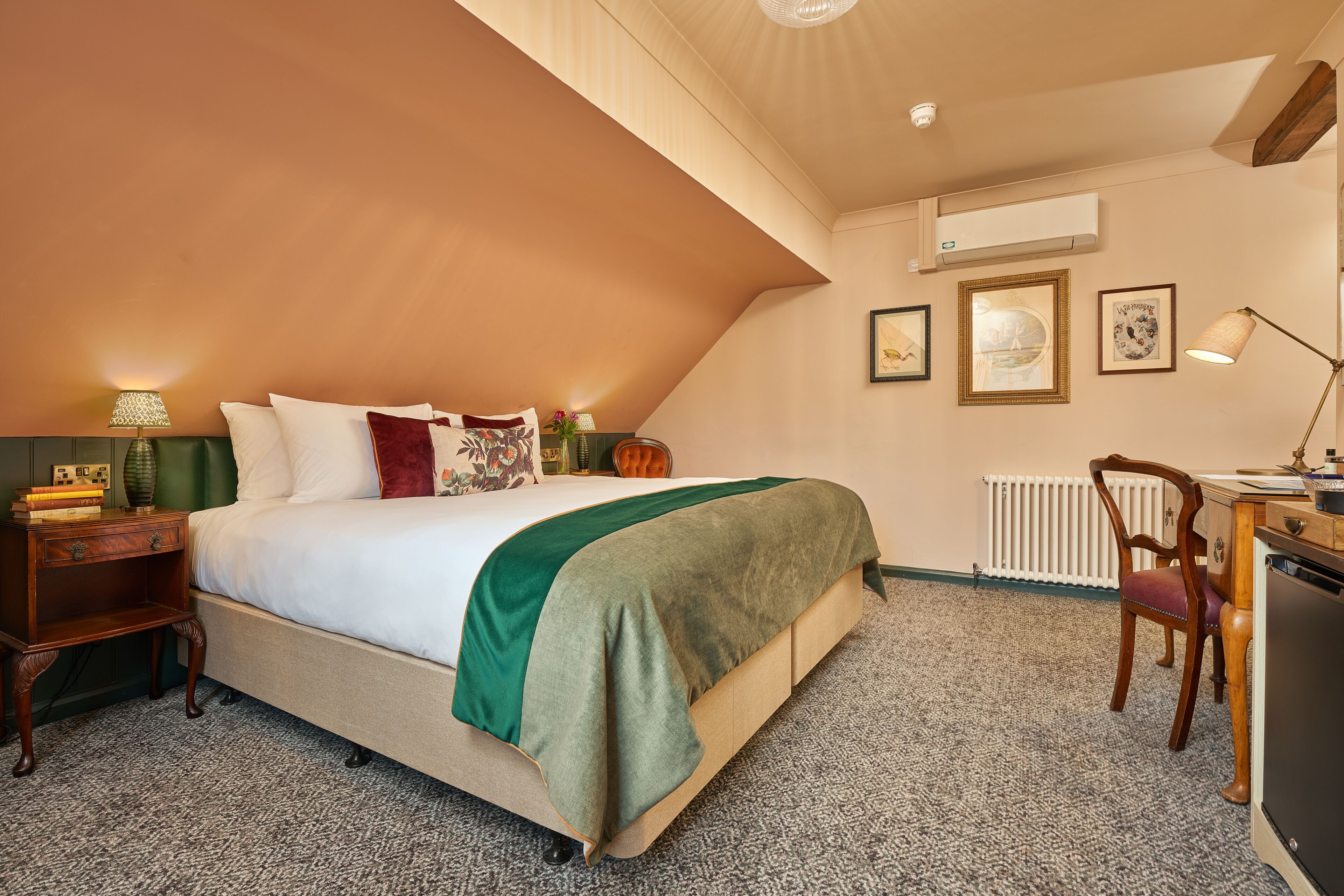A bedroom with a bed, bedside table, lamp, chair, desk, and wall-mounted air conditioning unit.