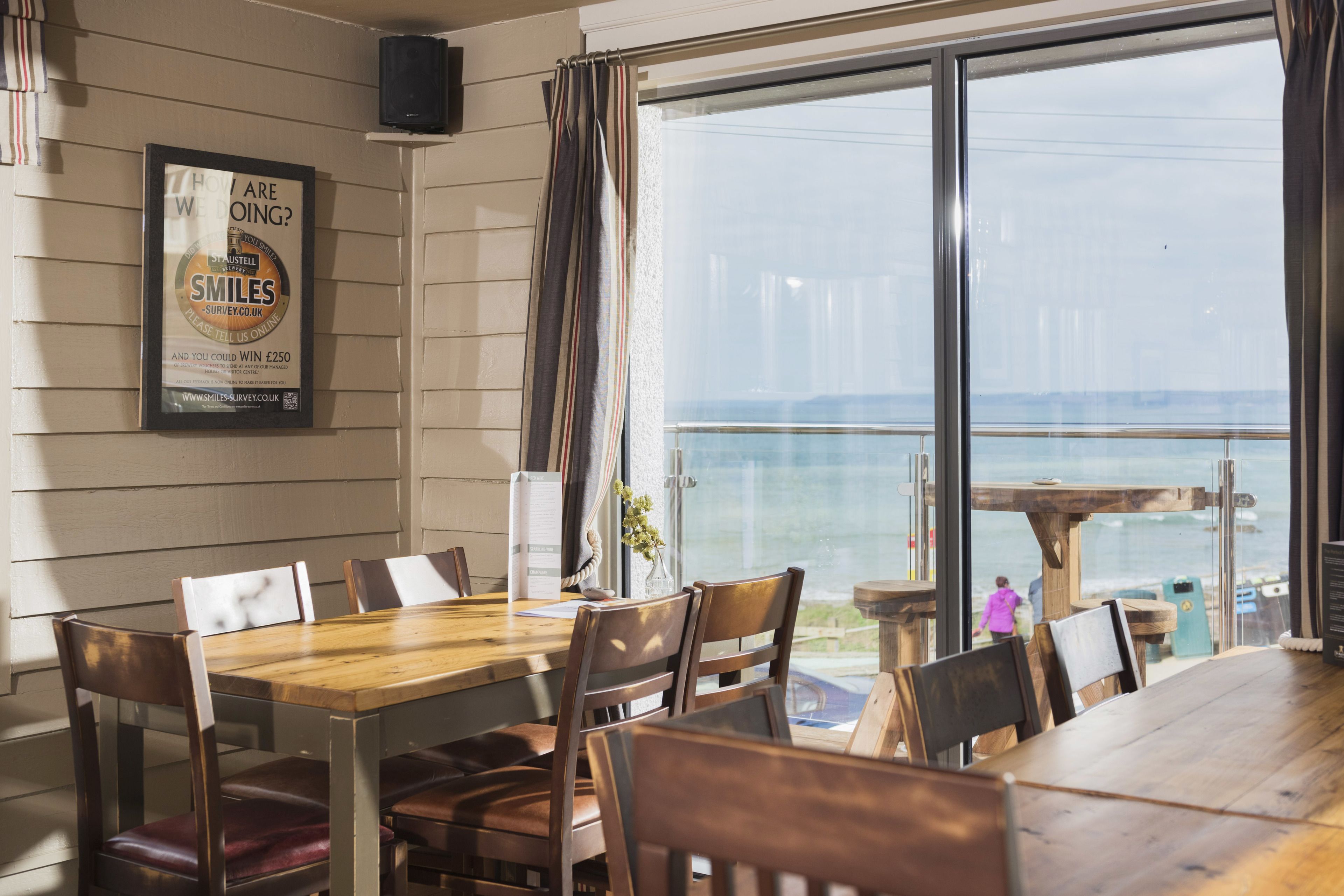 Un comedor con mesa y sillas de madera, un cartel enmarcado en la pared y vista al mar a través de amplios ventanales.