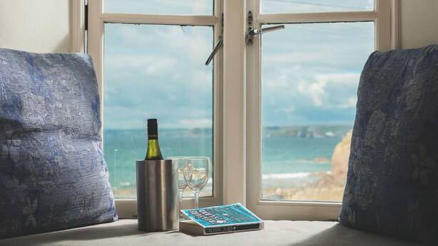 A window seat with a view of the ocean, a bottle, two glasses, and a book titled "Treasure Island". - Hope & Anchor (Kingsbridge)